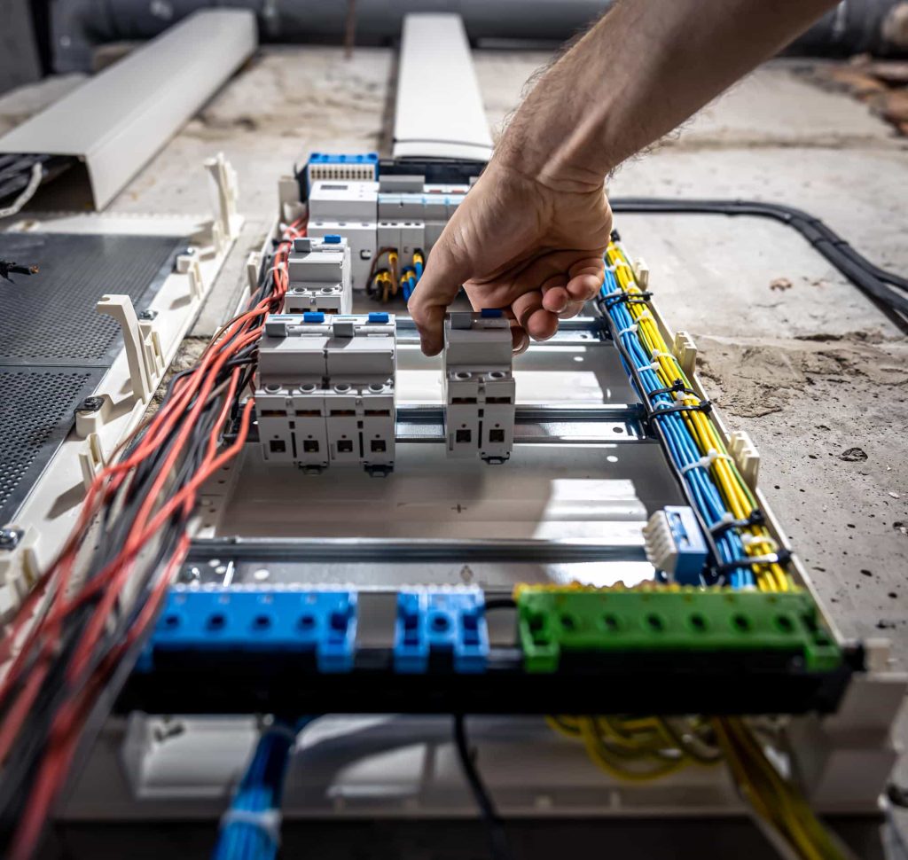 A person working on a large electrical panel, wearing safety gear and using tools.