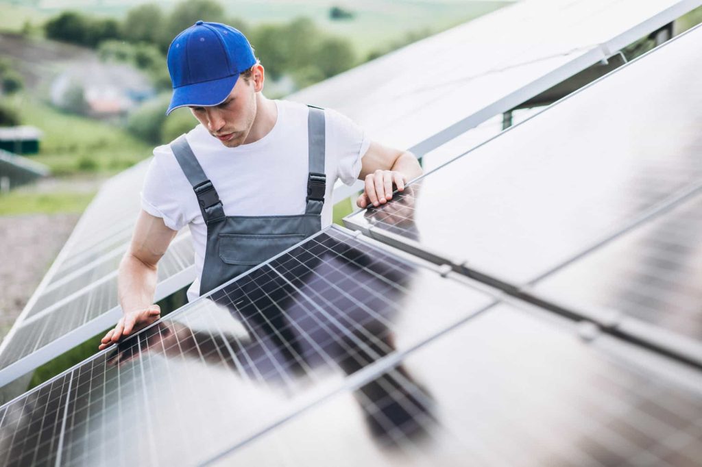 A man in overalls and a blue hat diligently works on a solar panel, harnessing renewable energy.