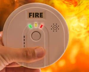 Person holding fire alarm in front of fire, ready to alert others of potential danger.